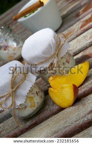 Two glasses of homemade yogurt with pieces of peach on an old wooden surface. Two pieces of peach in front.