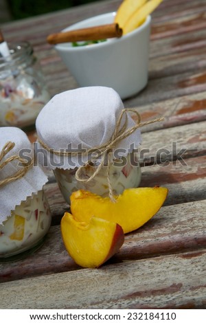 Two glasses of homemade yogurt with pieces of peach on an old wooden surface. Two pieces of peach in front.