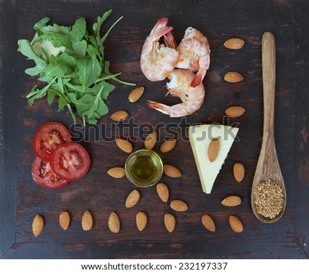 Rucola salad ingredients-rucola leaves, shrimps,almond nuts,tomatoes,sesame seeds,olive oil,cheese- on the old black wooden surface. Top view. Background