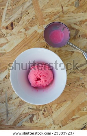 Red berries ice cream in a white plate and a ice-cream spoon on the wooden surface