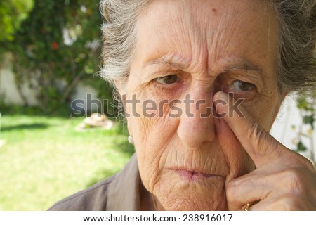 An old sad woman between 70 and 80 years old is drying the tears from her face. Garden background