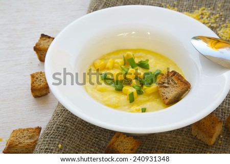 Light healthy soup- corn cream soup with green onion and croutons in a white plate on a grey sackcloth.
