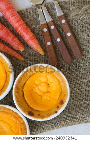 Homemade carrot cheese cakes in white ceramic moulds. Carrots and dessert spoons on a sackcloth