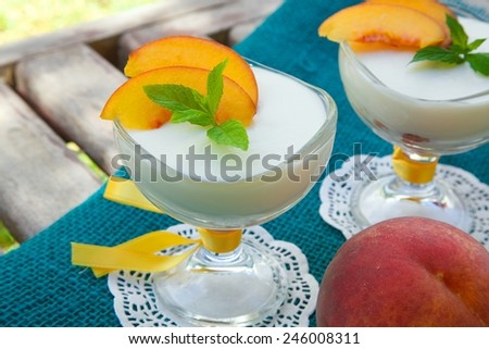 Milk dessert - sweet ricotta cheese with peach in a glass dessert bowl. Fresh peach in a background.