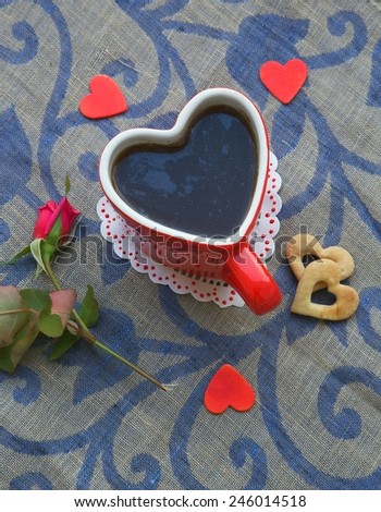 Prepared tea in cup of a heart shape. Red rose,red wooden hearts and biscuits are close to the cup