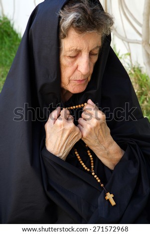 A senior woman between 70 and 80 years old, dressed in black, is praying in the garden