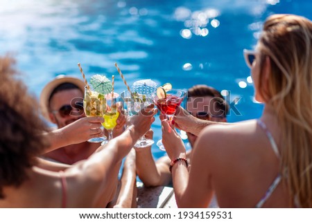 Friends drink cocktails by pool side on summer vacation and have fun together. People, love, summer, vacation and lifestyle concept.