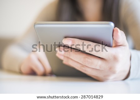 Woman is holding a digital tablet. The image is taken in the city. The young woman has long brown hair. The face of the  woman is not visible.