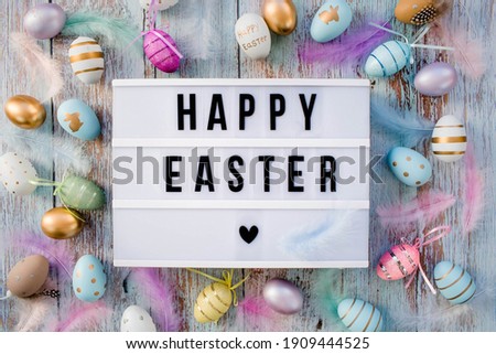 Stylish text frame of the lightbox with the inscription happy easter. Pink, blue, white, gold, and yellow eggs are everywhere. Colorful Easter eggs top view. Copyspace.