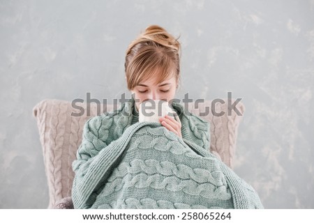 Attractive woman with natural blond hair posing without makeup with white cup of hot drink wrapped with blanket at home