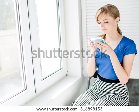 Attractive woman with natural blond hair with  cup of hot drink sitting near the window