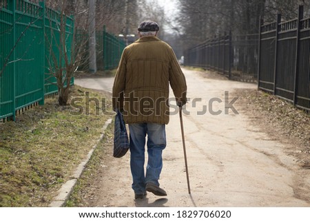 An elderly man with a stick is walking down the street. A man aged. The old grandfather is walking. The life of pensioners in Russia. Old age in the fall.
