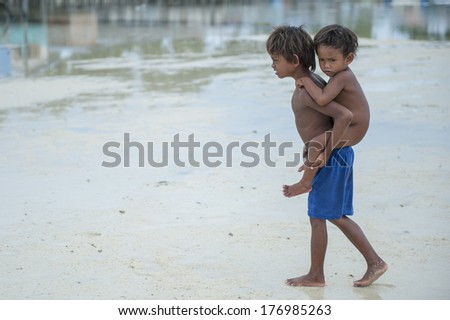 OMADAL ISLAND, SABAH, MALAYSIA - JANUARY 28 : Unidentified Sea Gypsies kid carry his brother on January 28, 2012 in Sabah, Malaysia.The Sea Gypsies are sea nomads that move from one place to another.