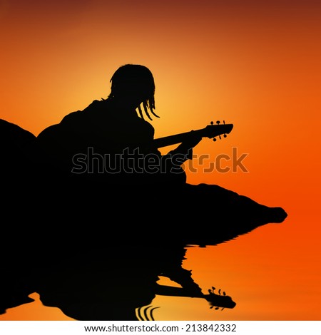 silhouette of rasta man playing guitar with water reflection