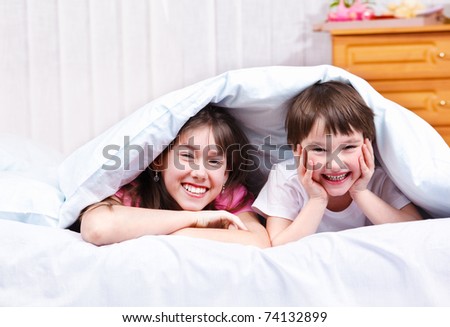 Brother and sister under blanket, laughing