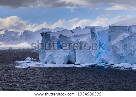 Beautiful blue ice cliffs and blue ice crevasses of a tabular blue iceberg from a melting tidewater glacier floating off the stunning Antarctic scenery of the Antarctic Peninsula of Polar Antarctica