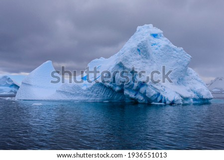 Close up view of Antarctic scenery with a blue iceberg and ripples in the blue sea under a grey sky with low cloud off Cuverville Island in Antarctica