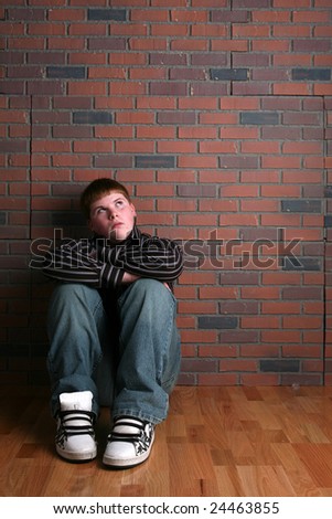 teenage boy sitting against a wall and depicting the concept of loneliness