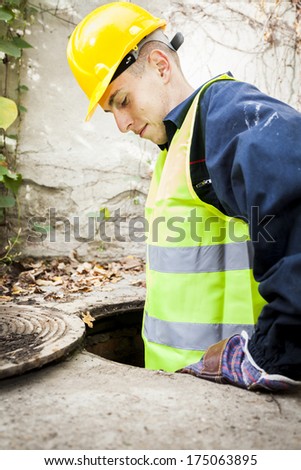 Manual worker entering manhole to fix the problem, half in drainage, looking down.