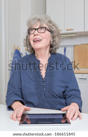 Cheerful old lady with touch pad in kitchen, having a good idea