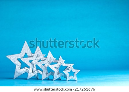 Silver shimmering stars in five different sizes on light blue background, copy space