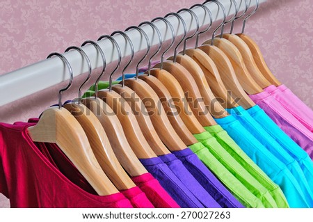 Pink, purple, crimson, bright green and turquoise women\'s T-shirts hanging on wooden hangers on pink background