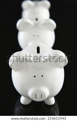 Row of white ceramic piggy banks receding back into the distance on a dark background with shallow dof and focus to the coin slot of the front pig in a financial concept