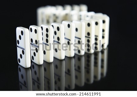 Curving row of dominoes standing upright on a reflective black surface conceptual of the domino effect - when one falls, all fall