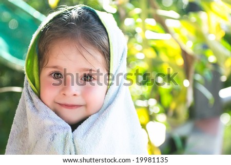 Headshot of a beautiful children wrapped in a towel showing a charming smile and sparkling eyes, on a green tropical background