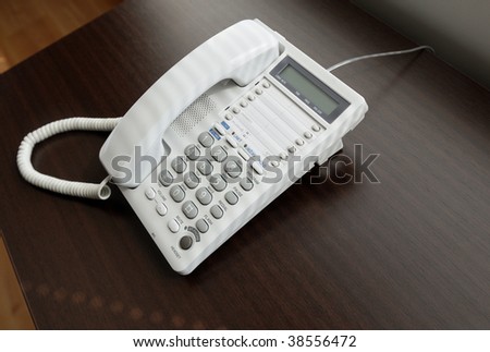 White office telephone over brown desk, with  light coming from a window