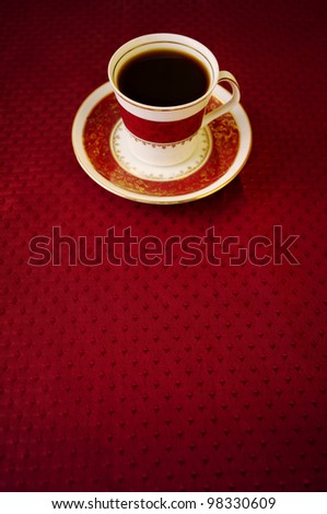 Vintage coffee cup with red and gold patterns over red carpet against yellow background a small coffee jar is blurred in the background. Dynamic angle accentuate the cup and give motion to the scene.