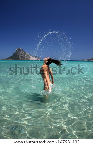 Beautiful young woman splashing water with her hair in the ocean.