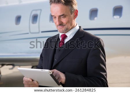 executive business man in front of corporate jet looking at tablet computer