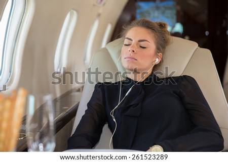 Business woman in a corporate jet relaxing and listening to music