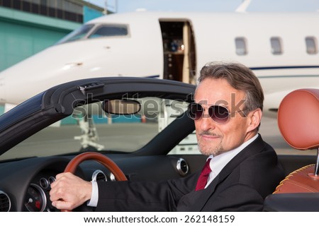 executive business man in a cabriolet in front of corporate private jet