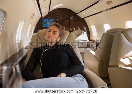 Business woman in a corporate jet relaxing and listening to music