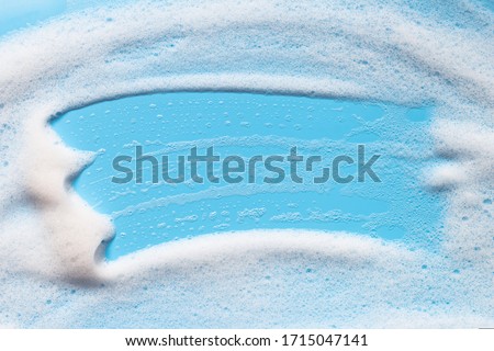 Shampoo foam on blue surface. Soap, shower gel, mousse bubbles.  Bath hygiene background. Abstract cleansing foam texture