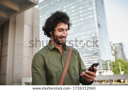 Handsome smiling young man in formal clothing using smartphone