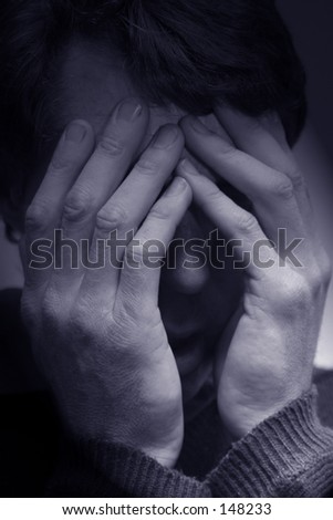Photo of a man holding his head.  Darkness surrounds him.