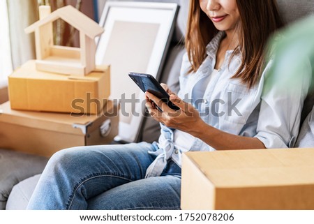 Happy young asian woman using smartphone in living room at new house with stack of cardboard boxes on moving day ストックフォト © 