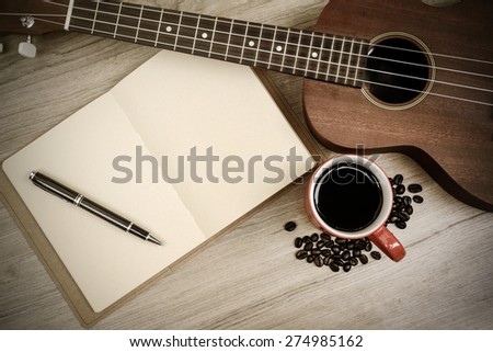 Cup of coffee with ukulele and notebook on wooden table, Vintage style