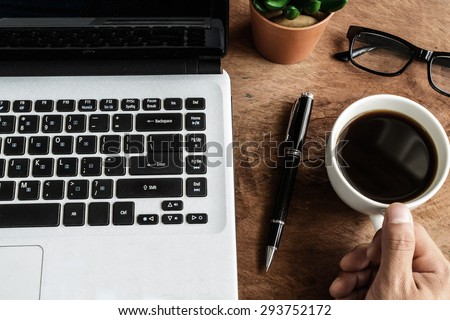 Laptop and cup of coffee with hand on old wooden table