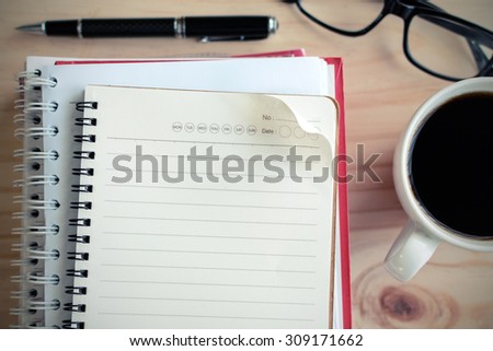 Cup of coffee with blank notebook on wooden desk, selective focus, Vintage tone