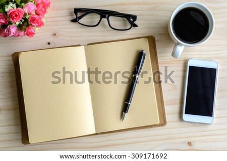 Cup of coffee with flower and blank notepad on wooden table