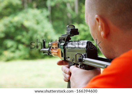 Man aiming at a target and shooting an automatic rifle for strikeball. Focus on the rifle sights.