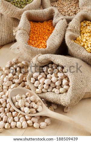 hessian bag with chickpeas and wooden spoon closeup; peas, wheat, red lentils and green mung on background