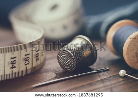 Sewing items - thimble, needle, measuring tape, spools of blue thread, including pins. Blue fabric for sewing on background. Stockfoto © 