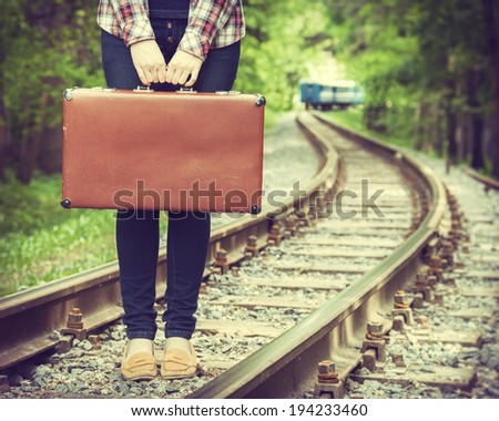 young woman with old suitcase on railway, departing train on background, retro stylized