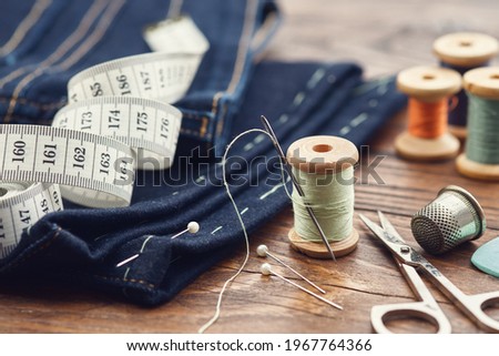 Shortening jeans. Measuring tape, scissors, spools of thread, thimble, including pins and chalk on table. Jeans cutting. Foto stock © 