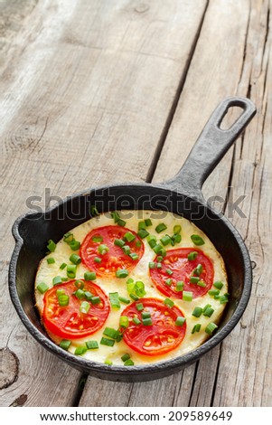 frying pan with scrambled eggs and tomatoes on wooden rustic table